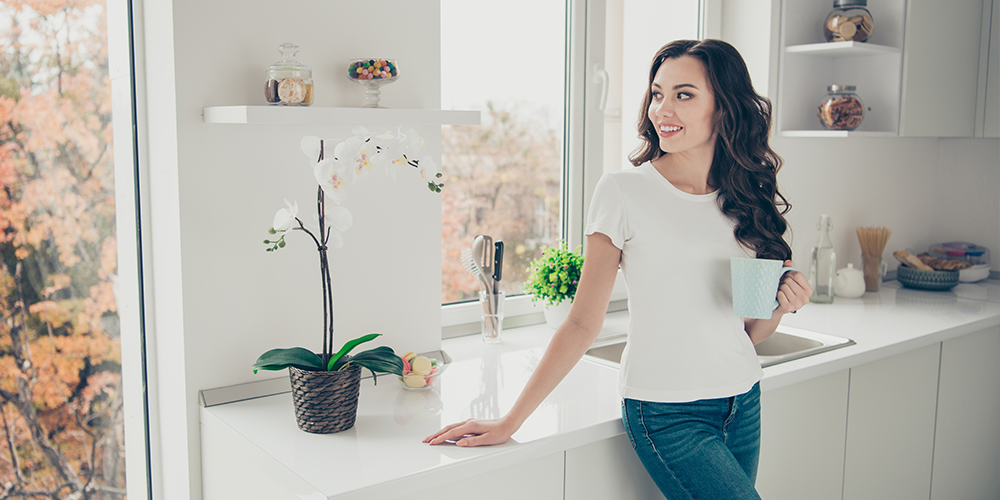 Thanks to a home air filter, a pretty homeowner enjoys clean air and a coffee in her clean kitchen.