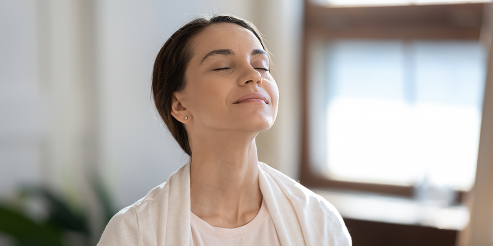 Young female homeowner breathes deeply and reaps great air purifier benefits.