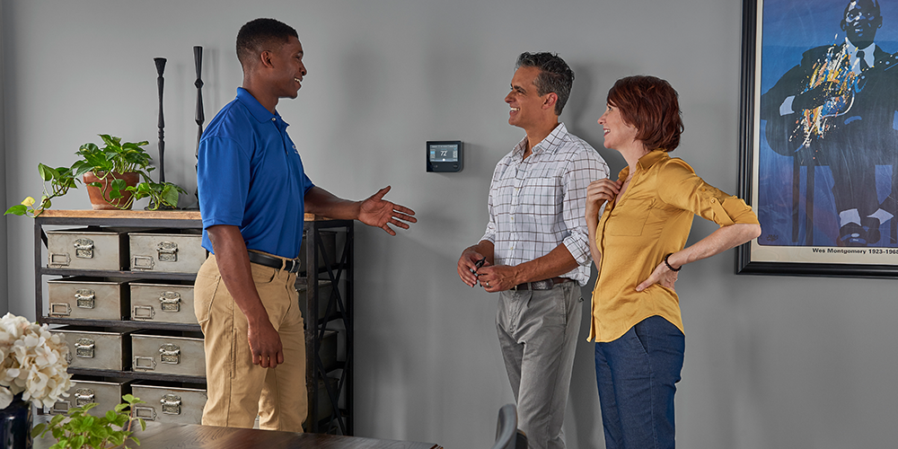 Tech in blue shirt shows homeowning couple HVAC troubleshooting tips in their home.