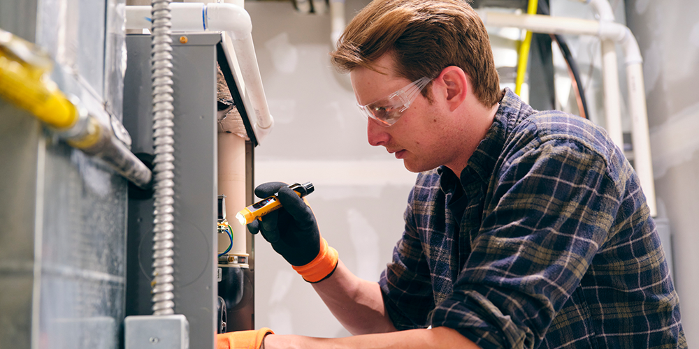 Tech with safety goggles inspects system to determine if a new furnace installation is necessary.