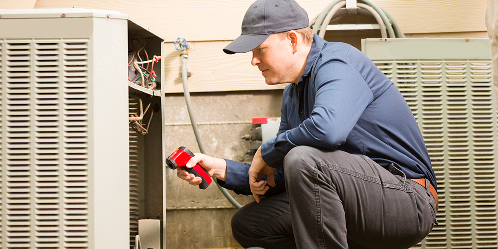 Tech in blue shirt and hat performs air conditioning maintenance on customer's A/C.