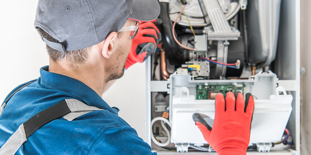 Technician looks inside heating system to determine when to replace a furnace.