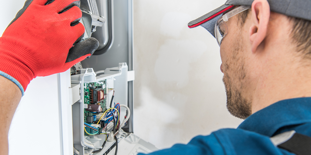 HVAC tech in hat performs residential furnace service for customer.