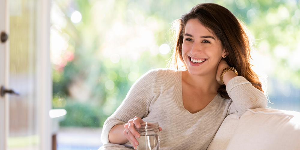 Young female homeowner sits on couch with glass of water after using air conditioning tips.