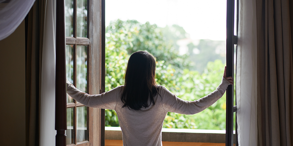 Woman opens wide windows to reduce indoor air pollutants.